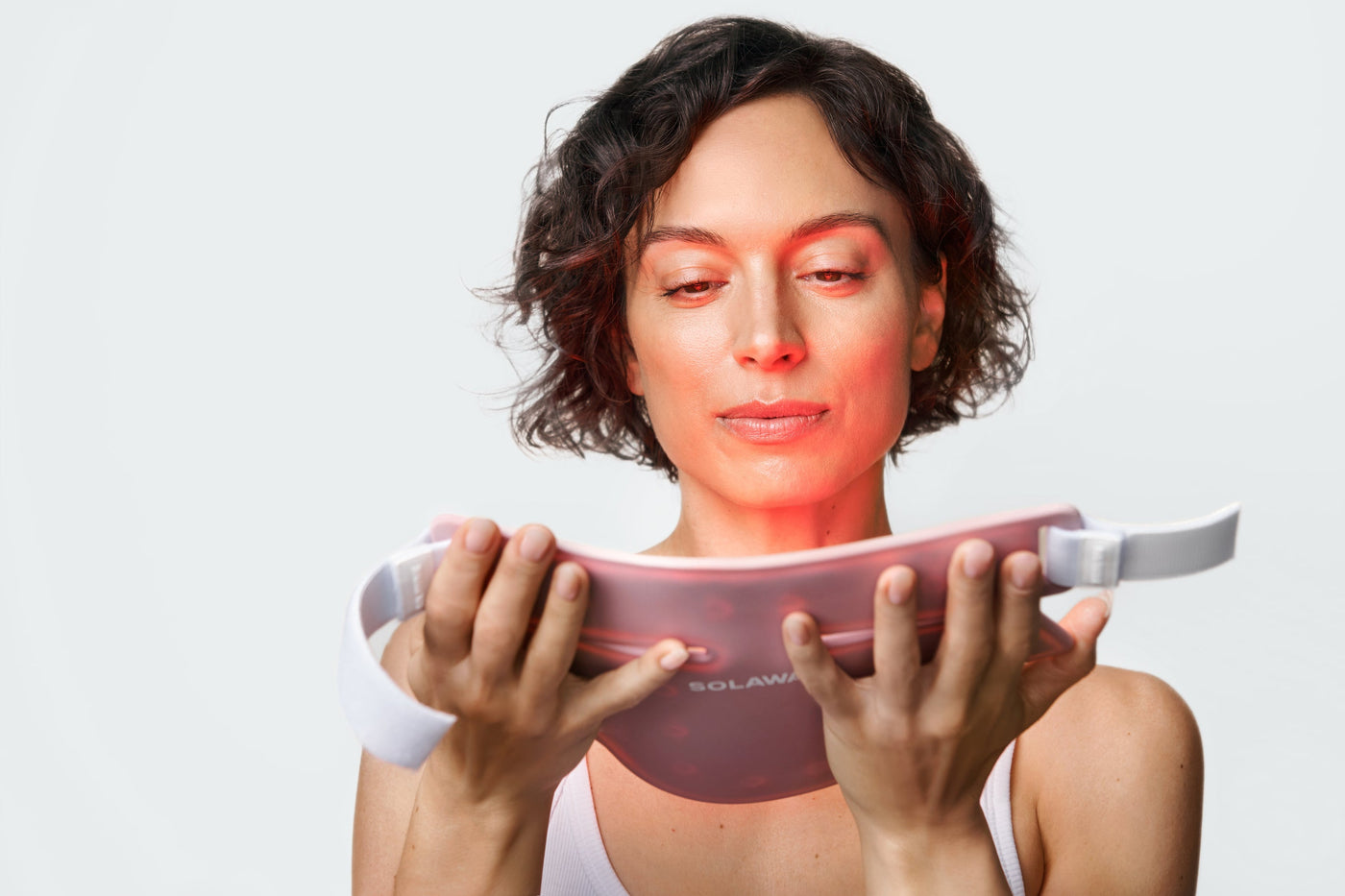 An image of a woman holding up a red light therapy face mask to her face