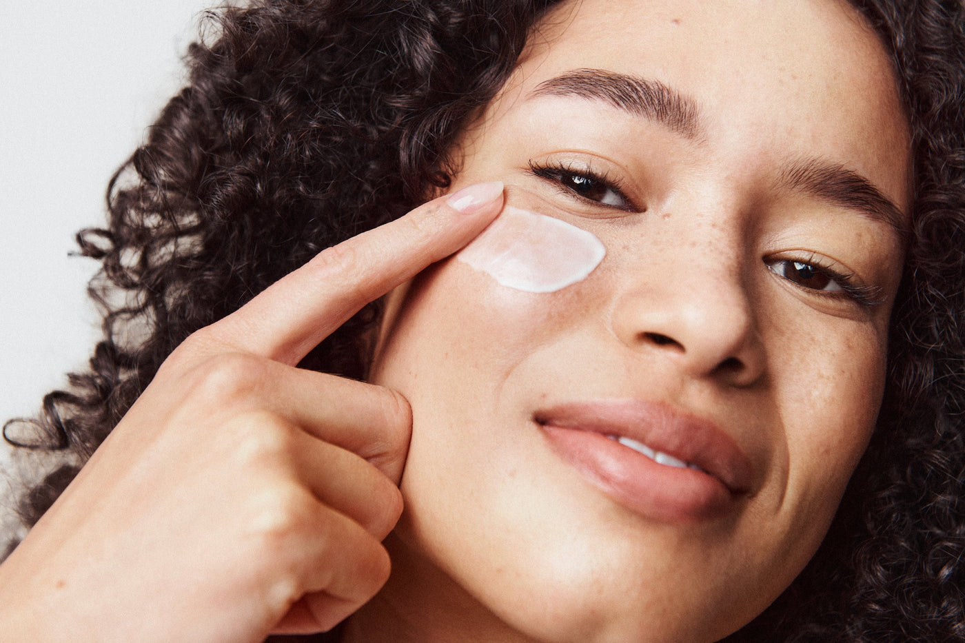 An image of a woman using under eye cream to combat dark circles under eyes