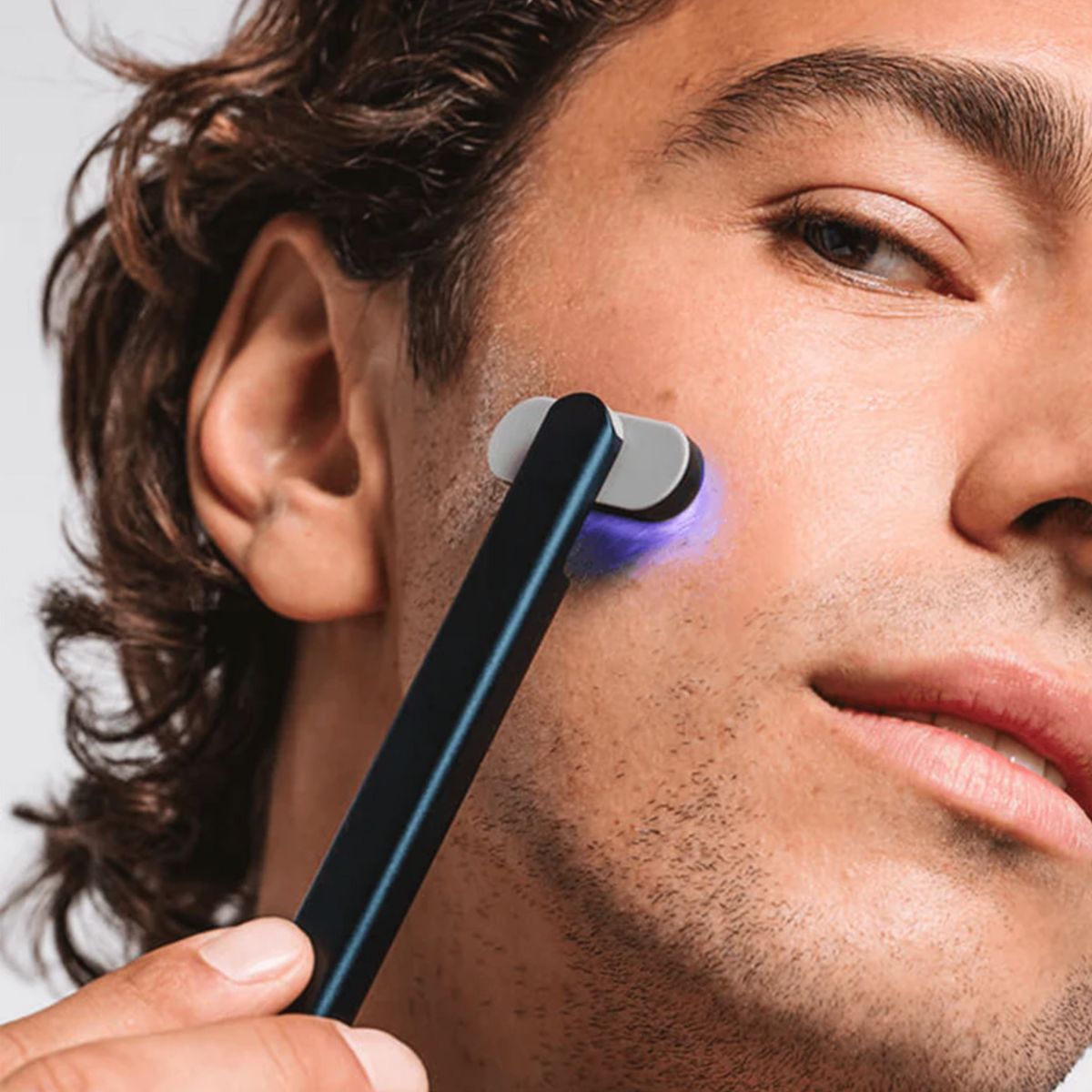 An image of a man using blue light therapy on his face