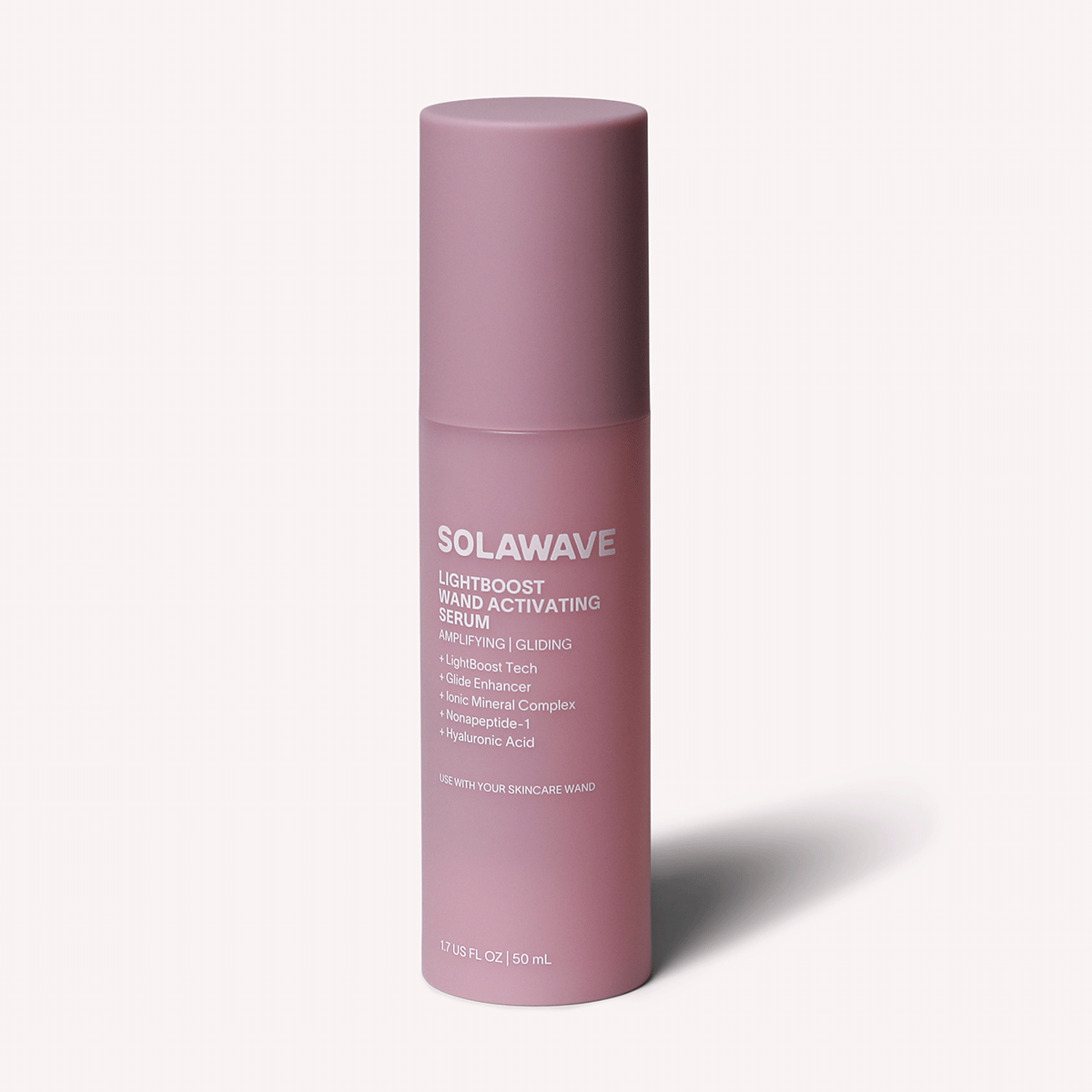 A pink cylindrical bottle labeled Solawave LightBoost Wand Activating Serum stands upright, featuring advanced LightBoost technology and contents like hyaluronic acid and plant extracts. It is set against a light pink background.