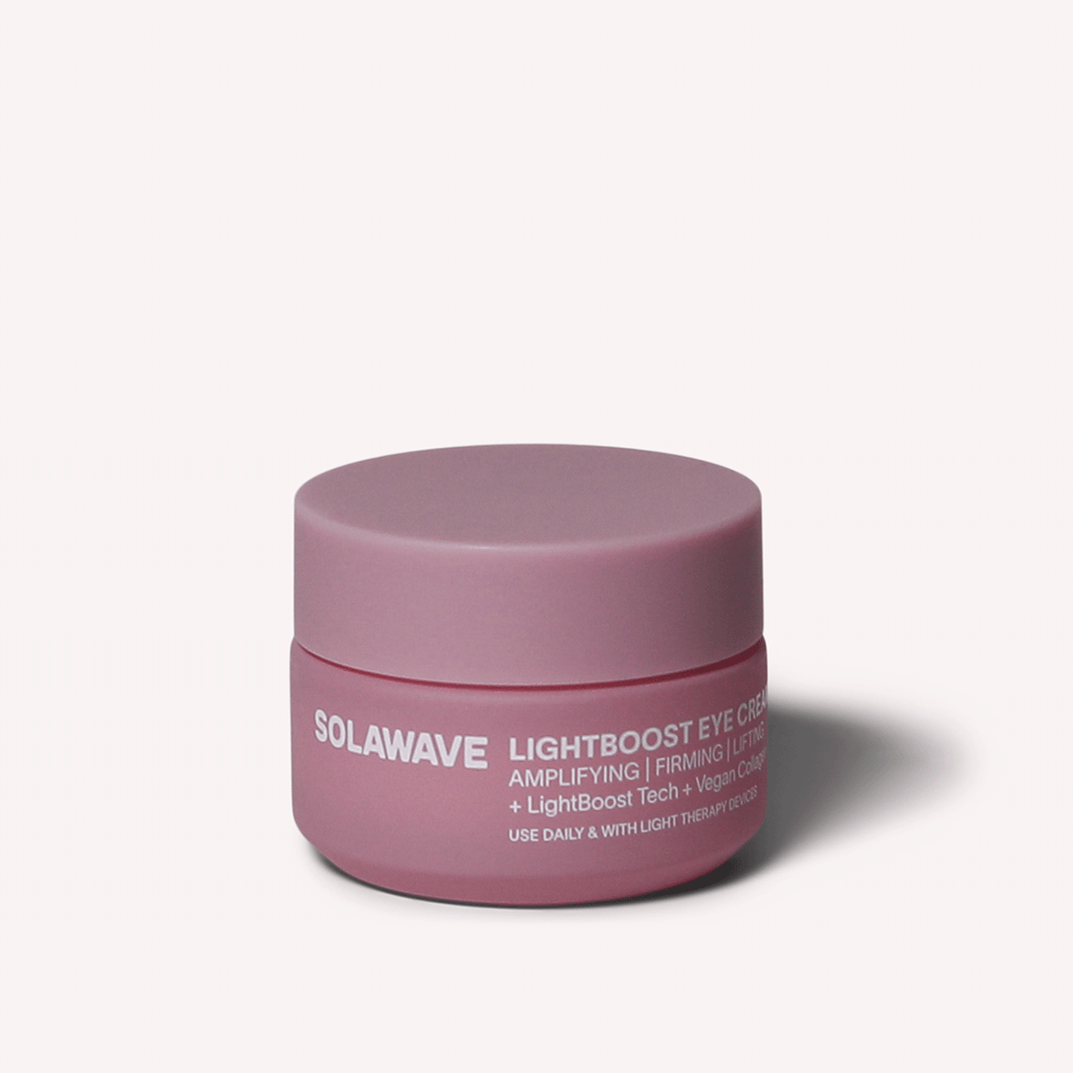 A pink round jar labeled Solawave LightBoost Eye Cream boasts benefits like amplifying, firming, and lifting with LightBoost Tech and vegan collagen, enhanced by light therapy. It features a matching lid against a soothing pale pink background.